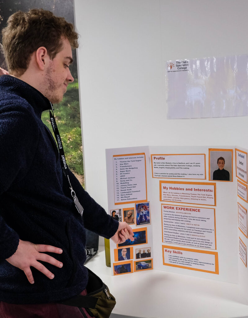 A male learner, looking towards a presentation board that he has made, showcasing his skills, interests and experiences