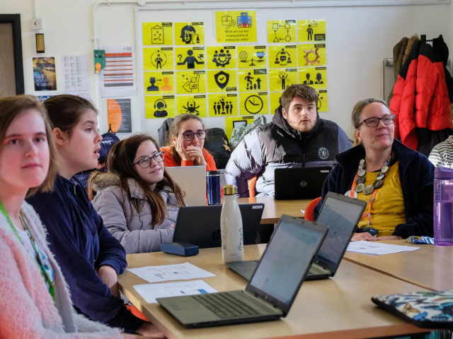 A group of learners and a staff member, in a classroom setting, listening intently