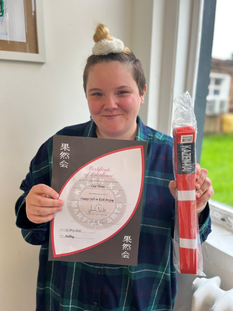 A young female learner proudly showing her certificate for excellence and orange belt in kick-boxing