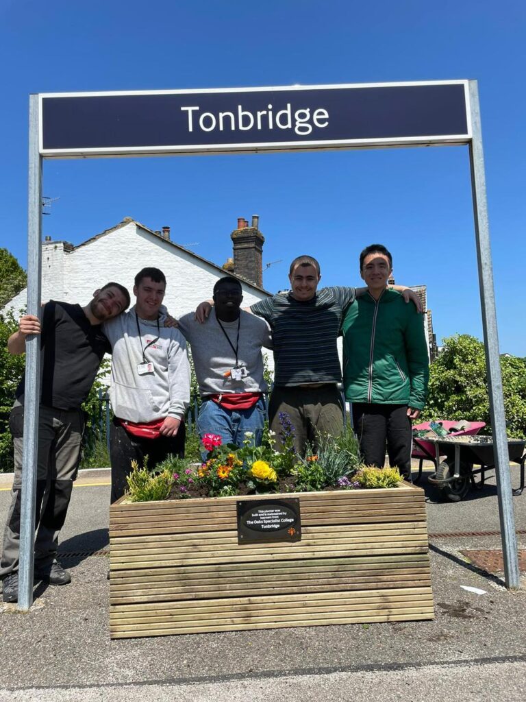 A group of learners standing, on a railway platform, behind the planter they made for Tonbridge train station