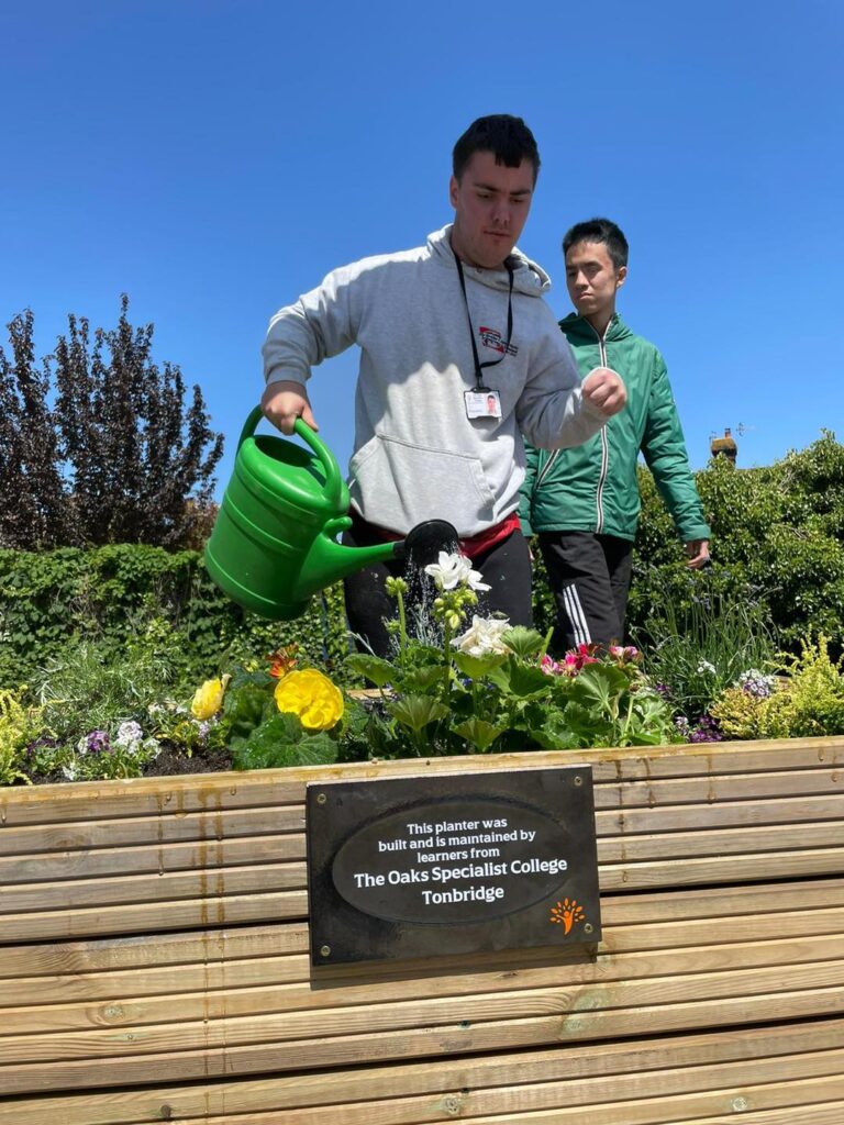 A young learner waters the planter, created by The Oaks carpentry enterprise group, at Tonbridge station