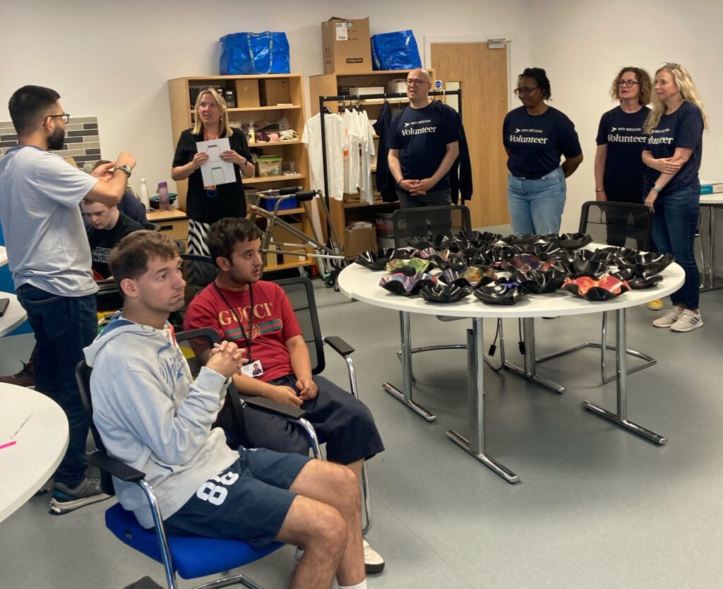 A group of corporate volunteers assisting a staff member and a group of learners, pictured behind a table of craft products made for the college shop