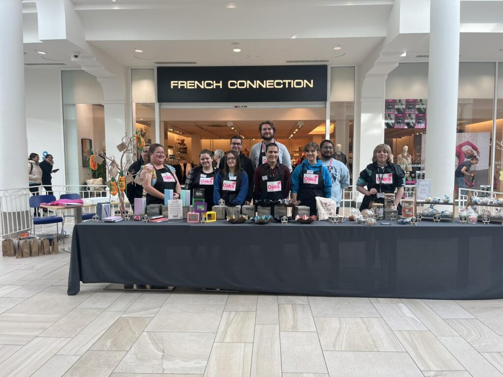 A big group of learners and staff standing in front of a display of their products at the Love That! pop-up shop in the Tunbridge Wells shopping centre