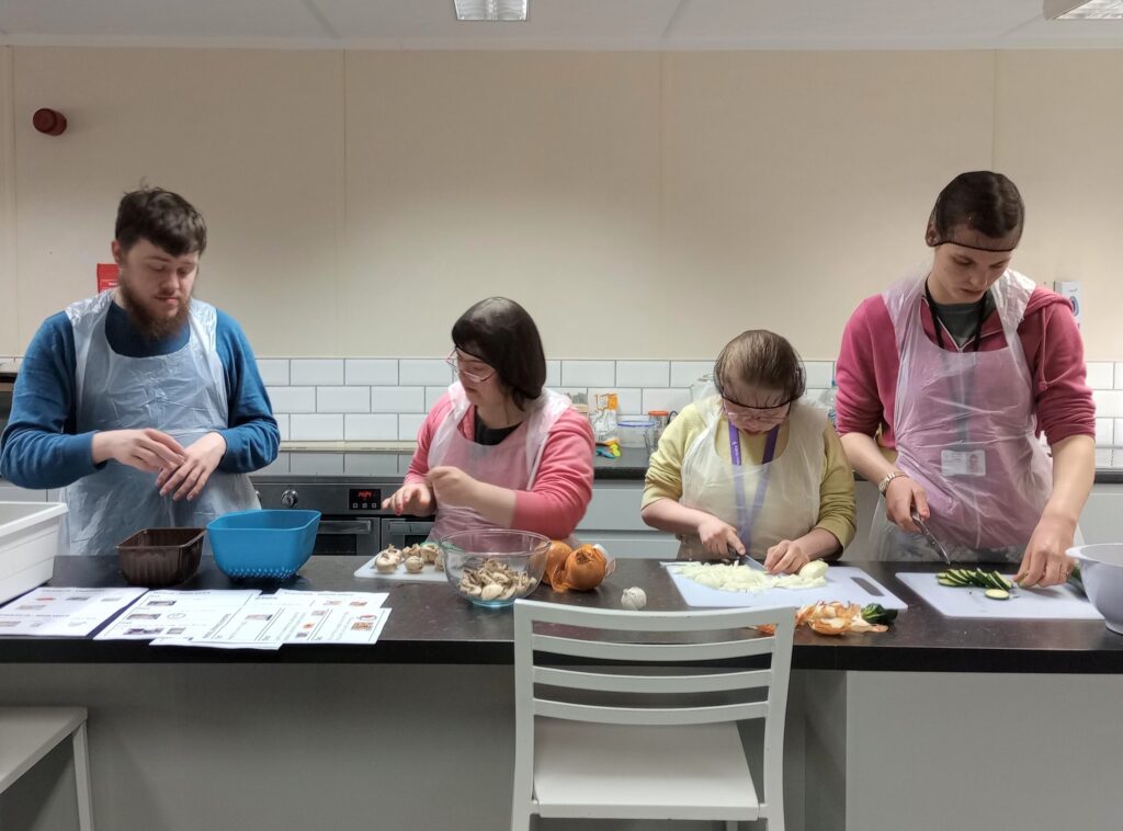 Four learners preparing food at a kitchen worktop