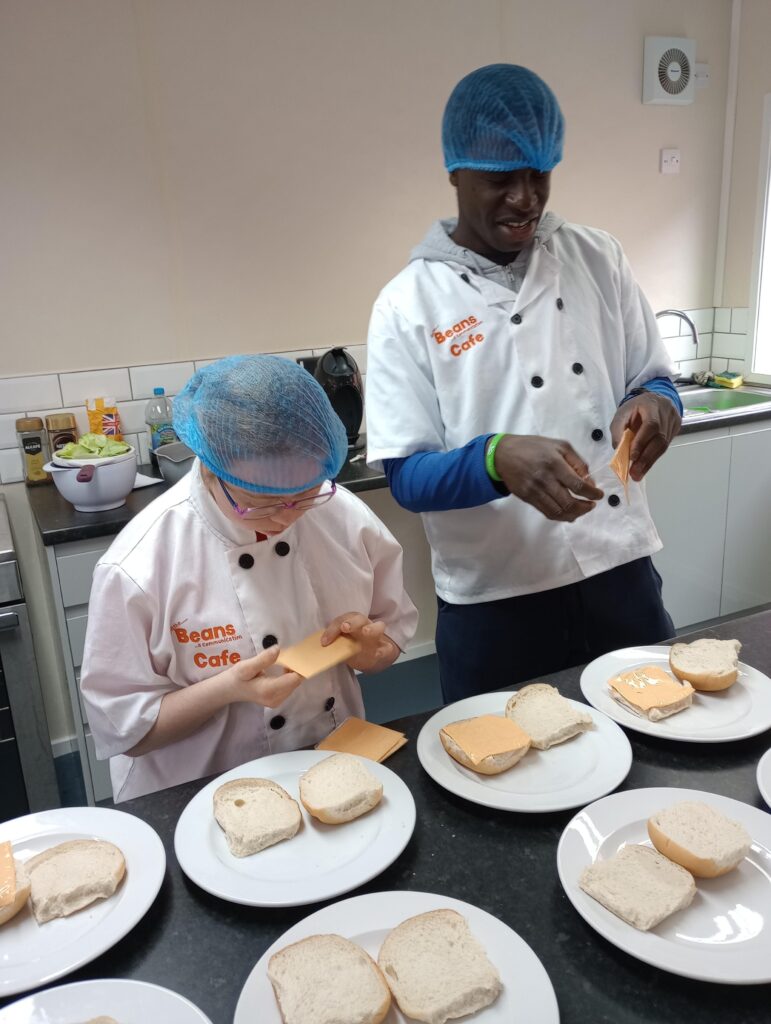 Two learners, dressed in chef whites, putting cheeseburgers together for a big lunch order