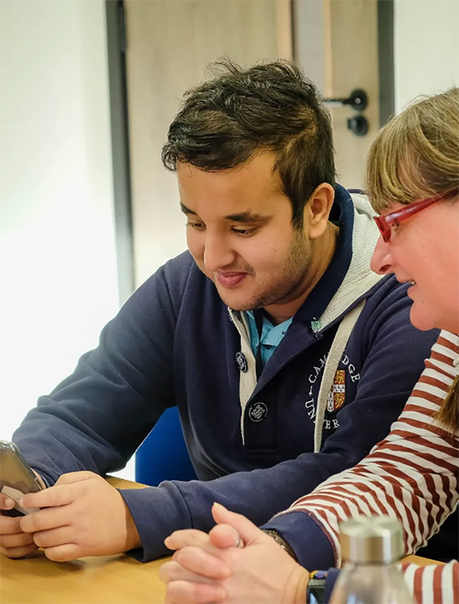 Photo of a male learner being shown how to access accessibility functions on his phone