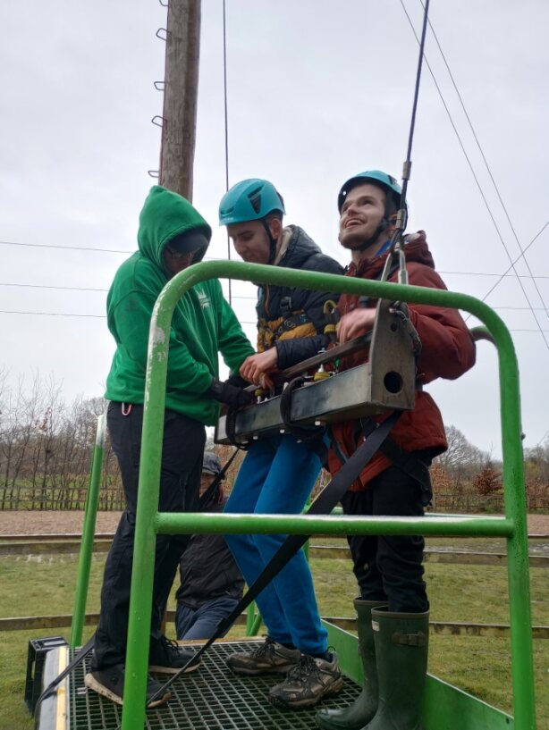 Two young learners being secured onto the safety harness of an assault course rope swing