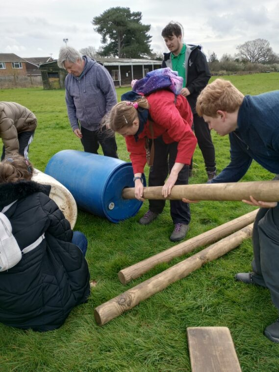 A group of young learners working together to build a structure with wooden stakes and empty oil drums