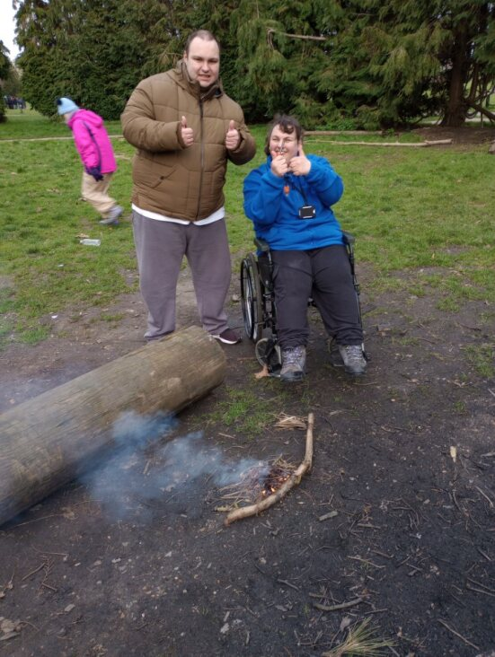 Two learners giving thumbs up signs to the camera, having lit a campfire