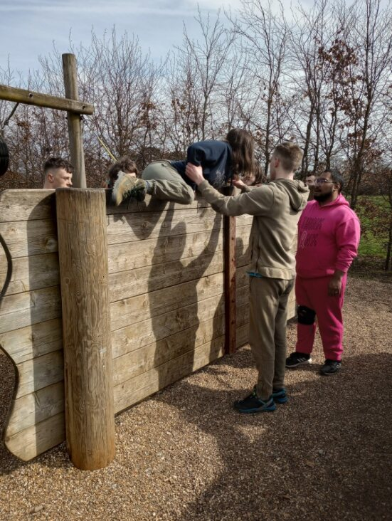 A group of learners supporting each other to climb over an assault course wall