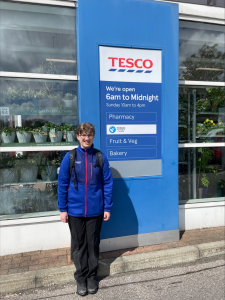 A young woman in Tesco uniform outside a Tesco Superstore, ready for her work shift.